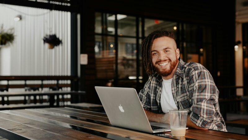 Leende man vid kafé bord med en plast kopp kaffe och laptop som vill veta hur man startar eget företag